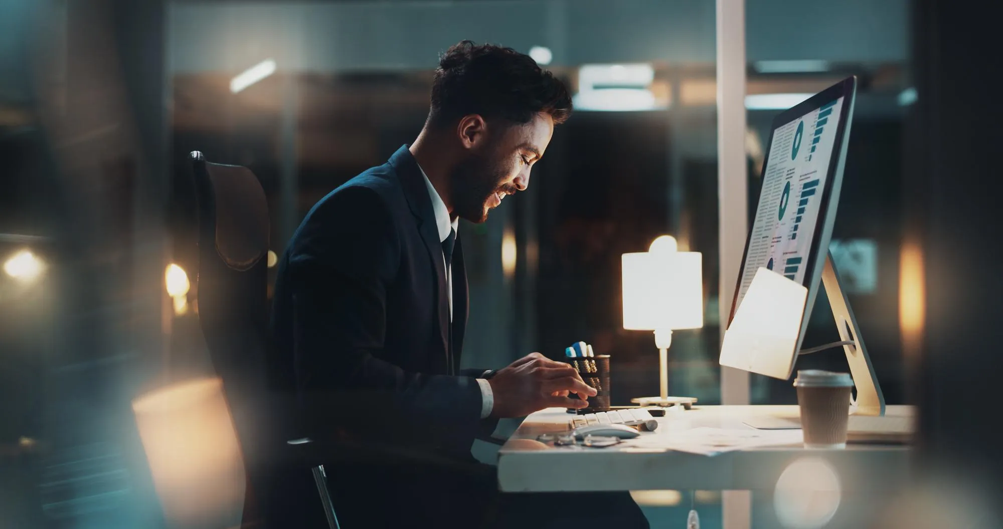 An accountant working late at a desk beside a computer screen.